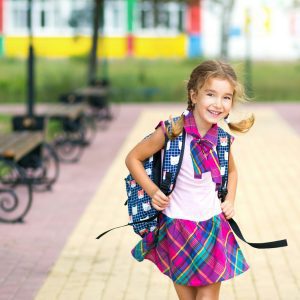 Cheerful girl with a backpack and in a school uniform in the school yard.