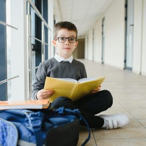 schoolboy sits on the floor of a school hallway and reads a book