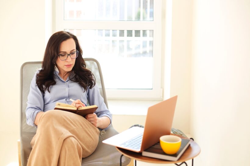 Adult businesswoman with laptop writing in notepad