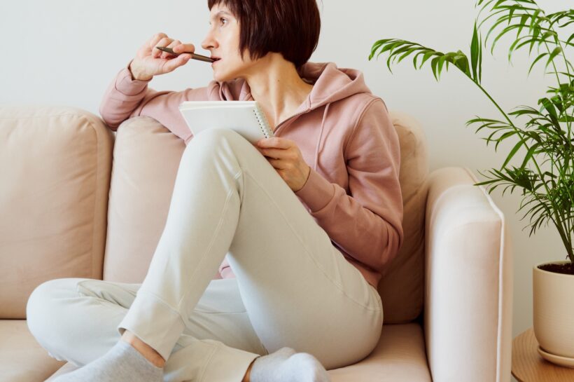 Mature female writing on to-do list notepad, mental health journaling, self-reflection