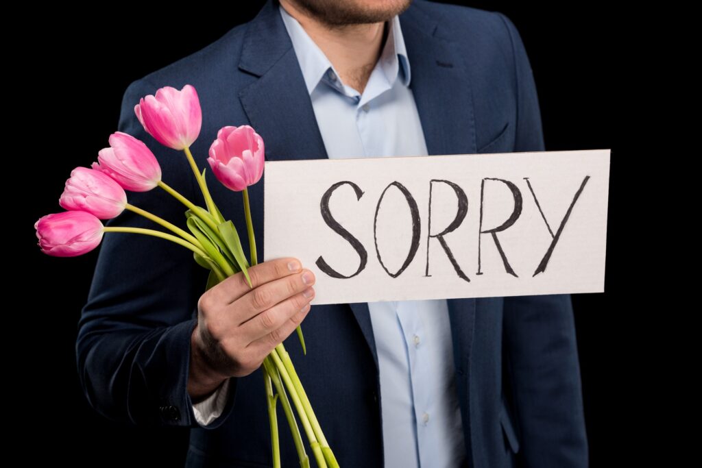 partial view of stylish man holding tulips bouquet and sorry sign isolated on black