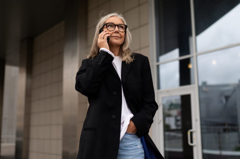 an elderly business woman enters the office center talking on a mobile phone, woman leader in