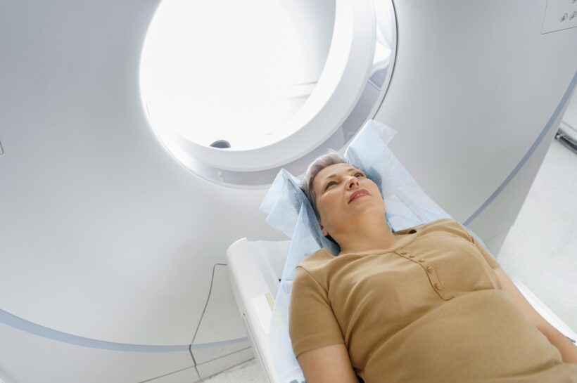 Female patient lying on table and entering CT machine during examination procedure in hospital