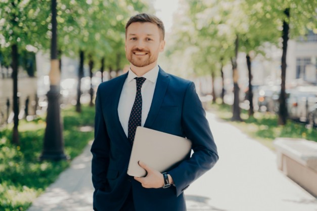 Businessman in suit walking on street holding laptop