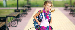 Cheerful girl with a backpack and in a school uniform in the school yard.