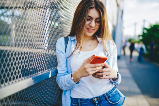 cheerful hipster girl share publication in blog using smartphone in city