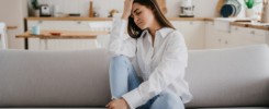 Exhausted brunette hispanic young adult woman in white shirt blue jeans sitting on sofa eyes closed