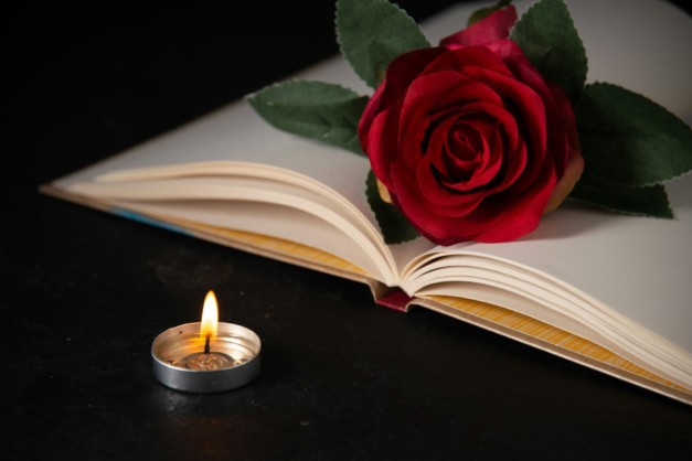 front view of burning candle with open book on dark background tank death