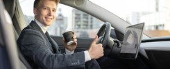 Handsome smiling Caucasian business man riding autonomous car, drinking coffee to go