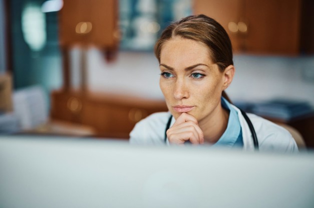 Pensive doctor working on her desktop PC at doctor's office.