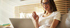 Portrait of laughing young woman sitting on bed with laptop chatting