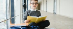 schoolboy sits on the floor of a school hallway and reads a book