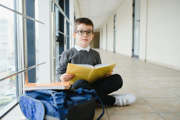 schoolboy sits on the floor of a school hallway and reads a book