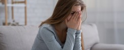 Young woman burying her face in hands and crying, feeling depressed or desperate on sofa indoors